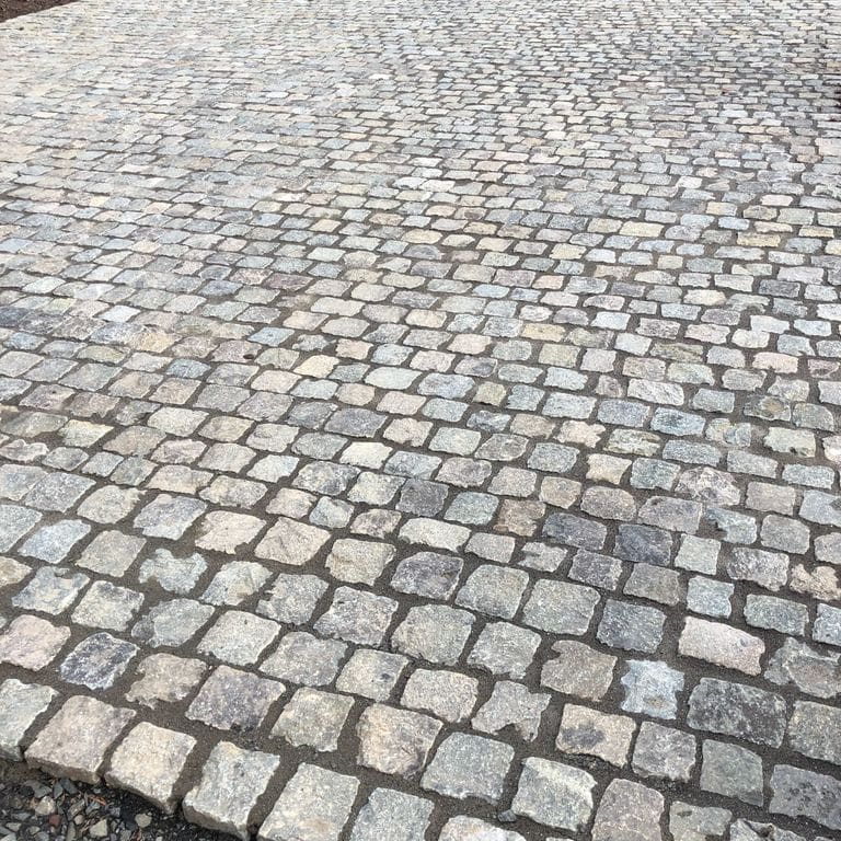 Application image for Reclaimed European Porphyry Cobblestones - Worn Cubes. The image shows this product being used for driveway pavers and patio pavers. The surface finish shown is . The dominant color shown is gray. The color mix creates a warm feeling.