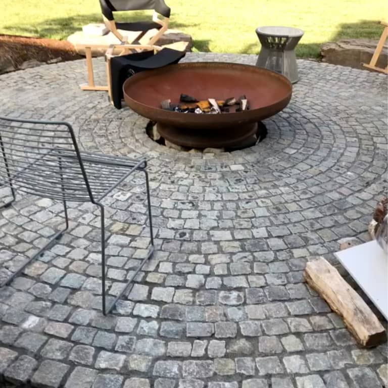 Application image for Reclaimed European Porphyry Cobblestones - Worn Cubes. The image shows this product being used in a patio pavers application. The surface finish shown is . The dominant color shown is gray. The color mix creates a warm feeling.