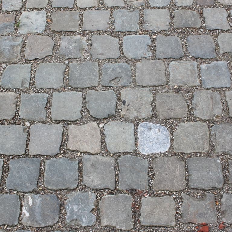 Application image for Reclaimed European Porphyry Cobblestones - Worn Cubes. The image shows this product being used in a path pavers application. The surface finish shown is . The dominant color shown is gray. The color mix creates a warm feeling.