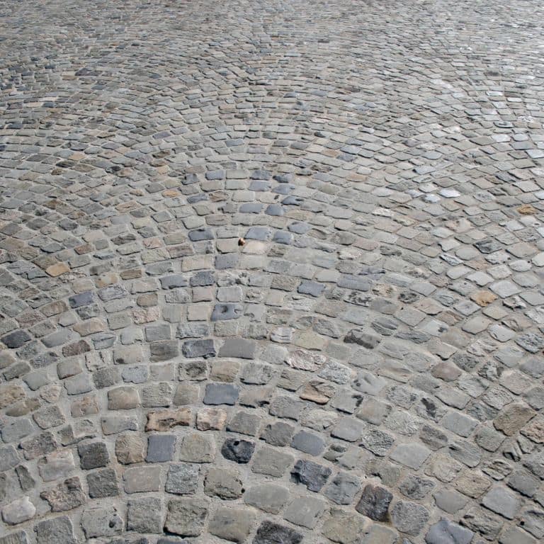 Application image for Reclaimed European Sandstone Cobblestones - Worn Cubes. The image shows this product being used in a driveway pavers application. The surface finish shown is . The dominant color shown is gray. The color mix creates a cool feeling.