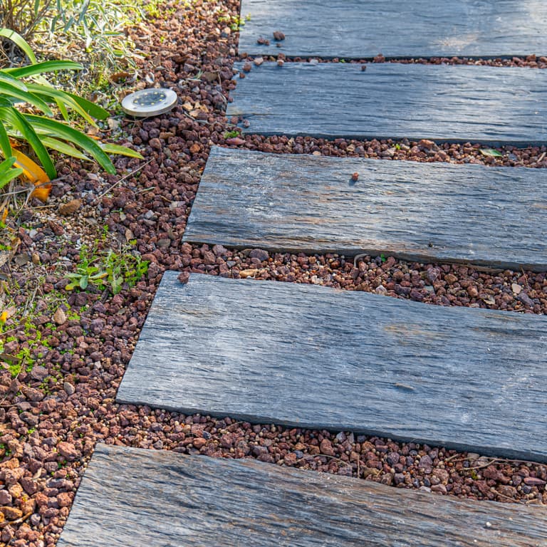 Best close-up image for Black Schist - Pavers. The image shows this product being used in a path pavers application. The surface finish shown is natural cleft. The dominant color shown is gray; with brown, green, purple, tan and cream secondaries. Exhibits "movement" and the color mix creates a cool feeling. Linear color pattern.