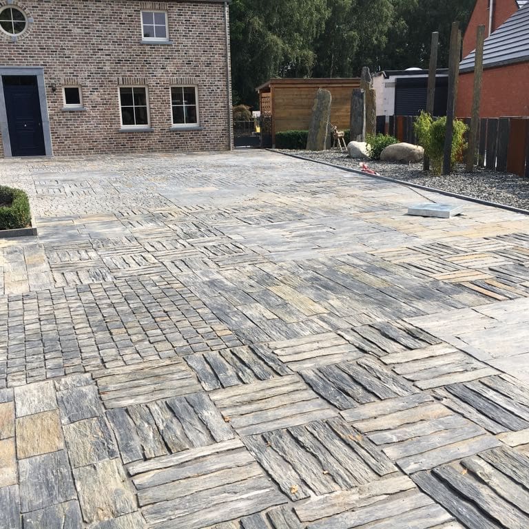 Application image for Black Schist - Pavers. The image shows this product being used for driveway pavers and patio pavers. The dominant color shown is gray; with beige, brown, orange/rust, white and cream secondaries. Exhibits "movement". Linear and streaked color patterns.