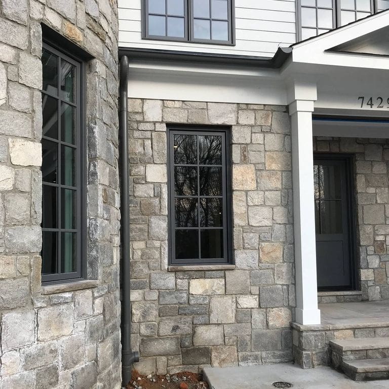 Feature image for Harbor Mist Granite - Wall Veneer. The image shows this product being used for full bed veneer and thin veneer. The dominant color shown is gray; with beige, purple, white, tan and cream secondaries. Exhibits "movement". Random, fine speckled, blotched, swirled and streaked color patterns.