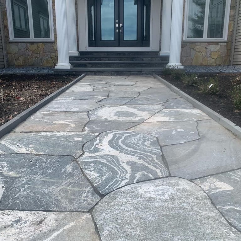 Feature image for American Mist Granite - Pavers. The image shows this product being used in a path pavers application. Dominant colors shown are blue and gray; with green and white secondaries. Exhibits "movement" and the color mix creates a cool feeling. Speckled, swirled and streaked color patterns.
