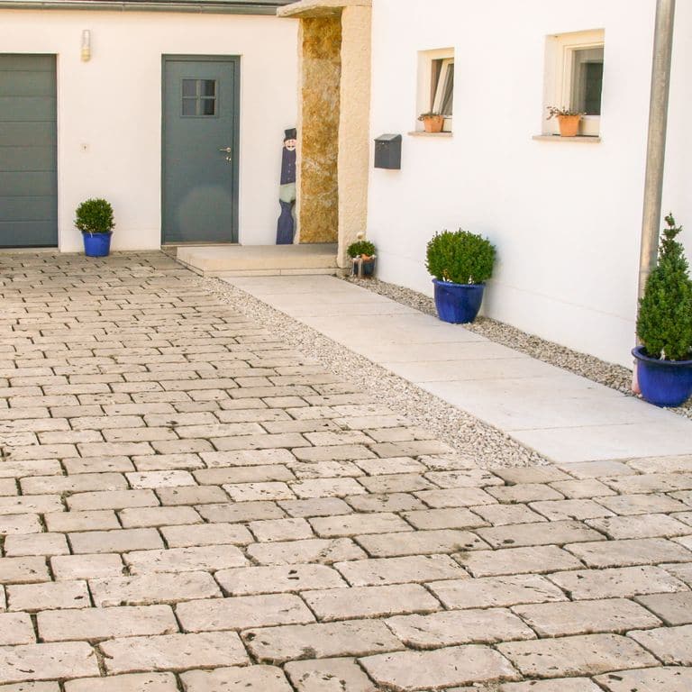 Application image for Bavarian Dolomite Gray Limestone - Cobblestones. The image shows this product being used in a driveway pavers application. Dominant colors shown are beige and tan. The color mix creates a warm feeling.