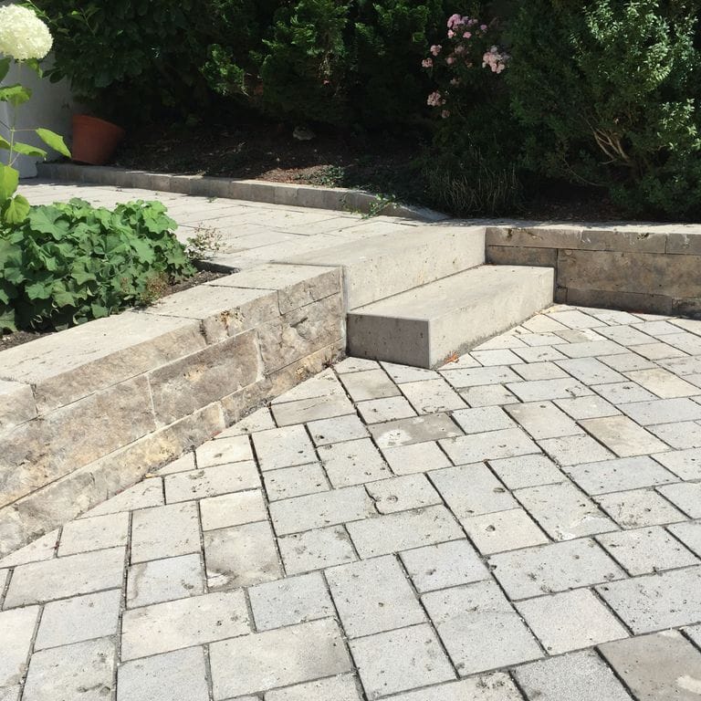 Application image for Bavarian Dolomite Gray Limestone - Cobblestones. The image shows this product being used in a patio pavers application. Dominant colors shown are beige, gray and tan. The color mix creates a warm feeling.