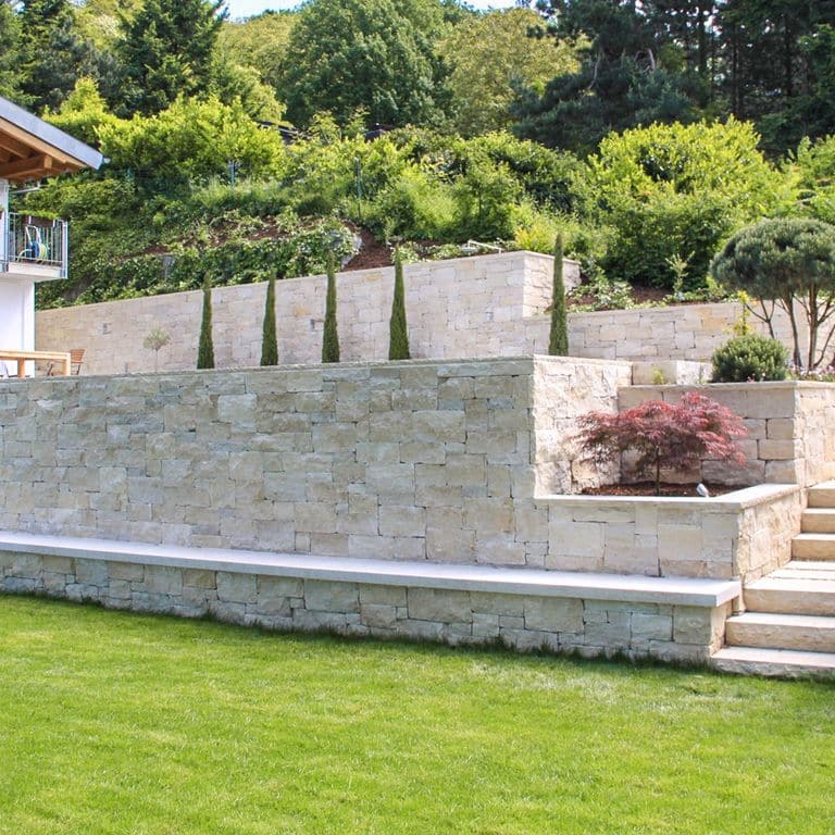 Application image for Bavarian Beige Limestone - Wallstone. The image shows this product being used in a landscape wallstone application. The surface finish shown is split-face. The dominant color shown is beige. The color mix creates a warm feeling.