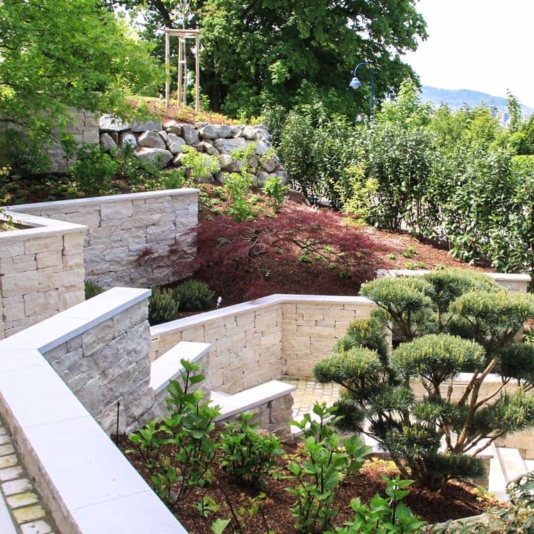 Application image for Bavarian Beige Limestone - Wallstone. The image shows this product being used in a landscape wallstone application. The surface finish shown is split-face. The dominant color shown is beige.