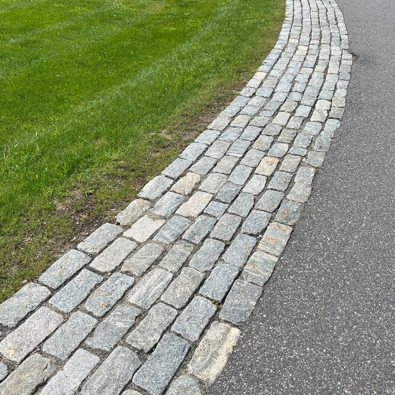 Application image for Granite - Cobblestones - Gray. The image shows this product being used in a driveway pavers application. The dominant color shown is gray. The color mix creates a cool feeling.