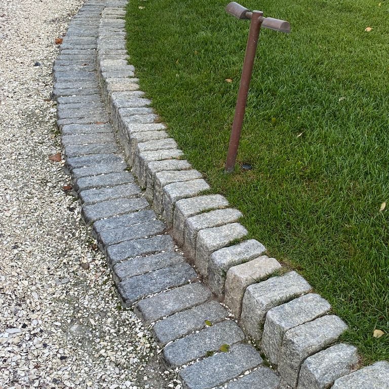 Application image for Gray Granite Cobblestone - Rectangles. The image shows this product being used in a landscape curbing &amp; edging application. The surface finish shown is tumbled. The dominant color shown is gray; with blue, green and white secondaries. The color mix creates a cool feeling. Speckled and coarse speckled color patterns. Contains some mica and mineral inclusions.