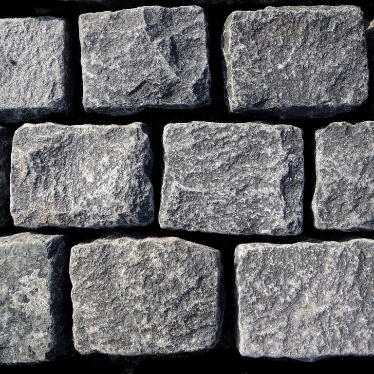 Feature image for Black Granite Cobblestones - Rectangles. The surface finish shown is split-face with flat plane. The dominant color shown is gray; with blue, green and white secondaries. Exhibits "movement" and the color mix creates a cool feeling. Regular and blotched color patterns. Contains some mica.