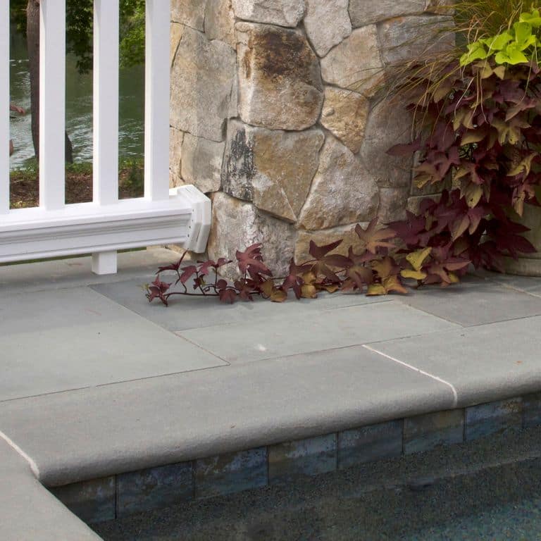 Best close-up image for Blue/Gray Bluestone - Flamed Pool Coping. The image shows this product being used for pool coping and pool deck pavers. The surface finish shown is flamed. The dominant color shown is gray. The color mix creates a cool feeling. Solid color pattern.