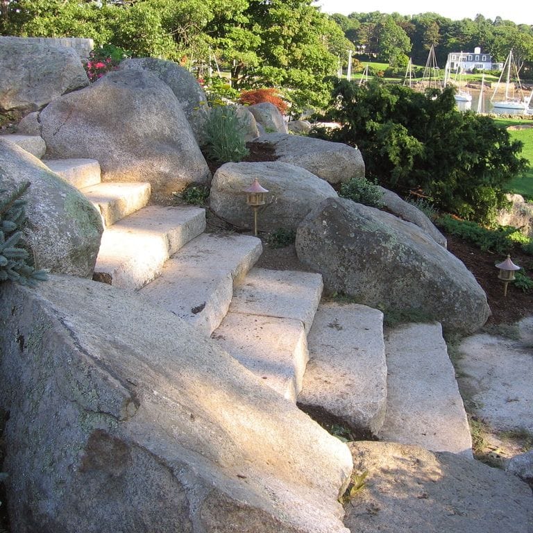 Application image for New England Fieldstone Boulders &amp; Ledgestone - Jumbo Boulders. The image shows this product being used for garden accents and landscape boulders &amp; ledge. The surface finish shown is weathered. The dominant color shown is gray. The color mix creates a warm feeling.