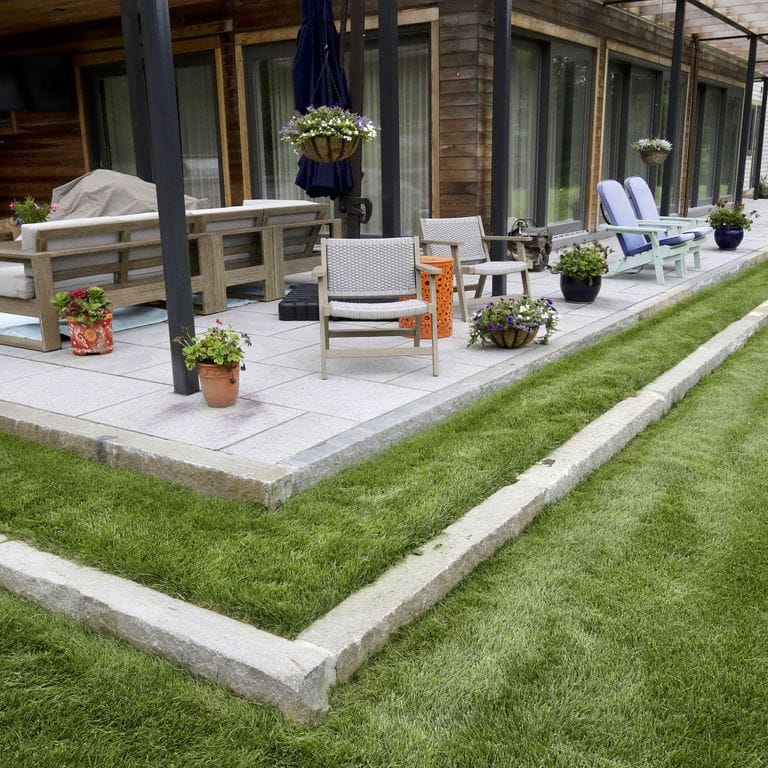 Feature image for Reclaimed Third Generation Granite Curbstone - Lawn Steps. The image shows this product being used in a landscape curbing &amp; edging application. The surface finish shown is . The dominant color shown is gray; with beige, white and cream secondaries. The color mix creates a cool feeling. Speckled color pattern.