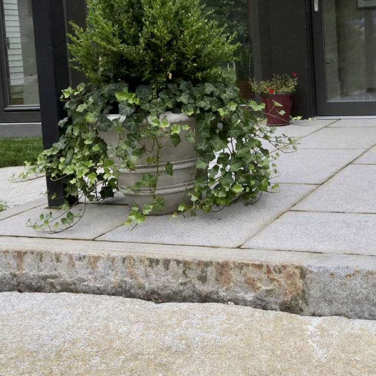 Close-up image for Reclaimed Third Generation Granite Curbstone Edging. The surface finishes shown are sawn, split-face with flat plane, weathered and worn. The dominant color shown is gray; with beige, brown, orange/rust, purple, white, tan and cream secondaries. Exhibits "movement". Random, speckled and blotched color patterns.