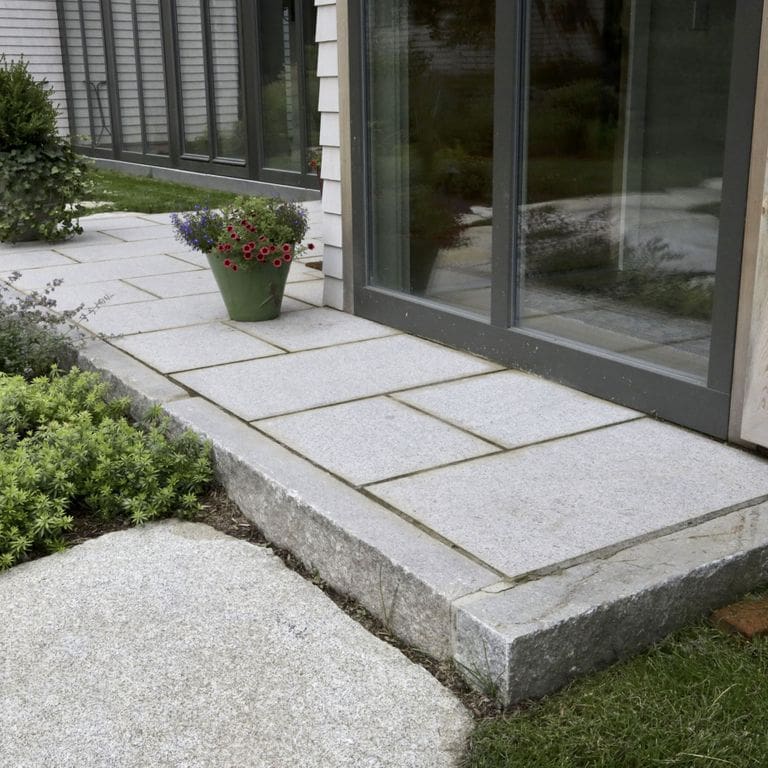 Feature image for Reclaimed Third Generation Granite Curbstone Edging. The image shows this product being used in a landscape curbing &amp; edging application. Dominant colors shown are gray and white; with beige and orange/rust secondaries. The color mix creates a cool feeling. Speckled and blotched color patterns.