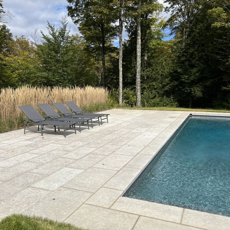 Feature image for Limestone - Madison - Pavers. The image shows this product being used for pool coping, patio pavers and pool deck pavers. The surface finish shown is flamed. The dominant color shown is gray; with purple, white and cream secondaries. The color mix creates a cool feeling. Regular color pattern.