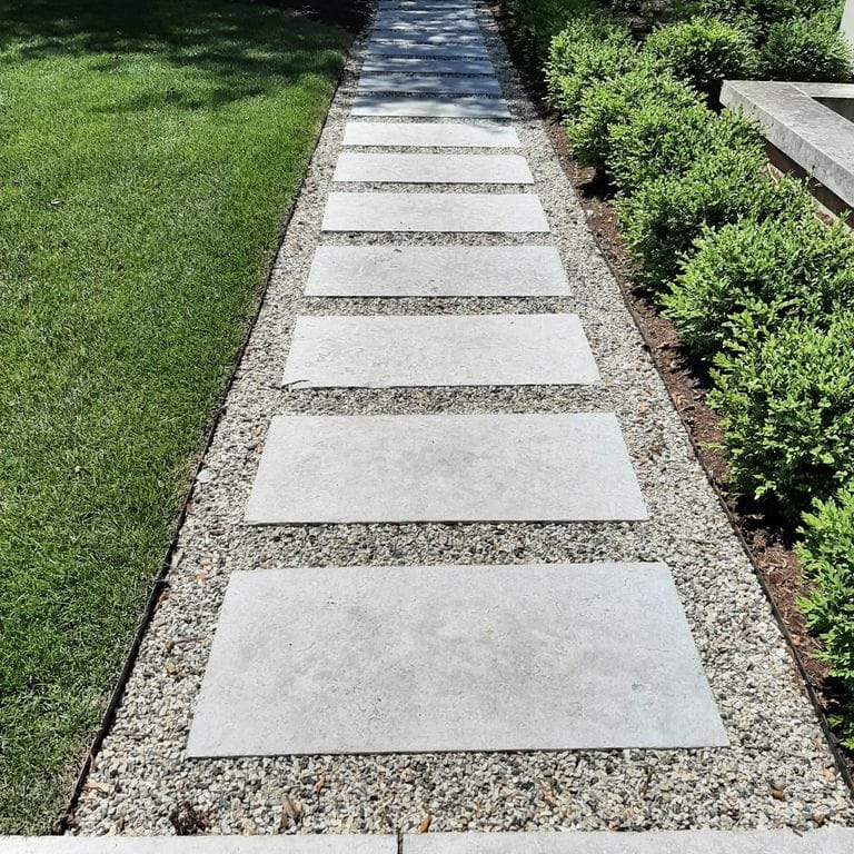 Application image for Madison Limestone - Pavers. The image shows this product being used in a path pavers application. The surface finish shown is flamed. Dominant colors shown are beige, gray and white; with a purple secondary. The color mix creates a cool feeling. Regular color pattern.