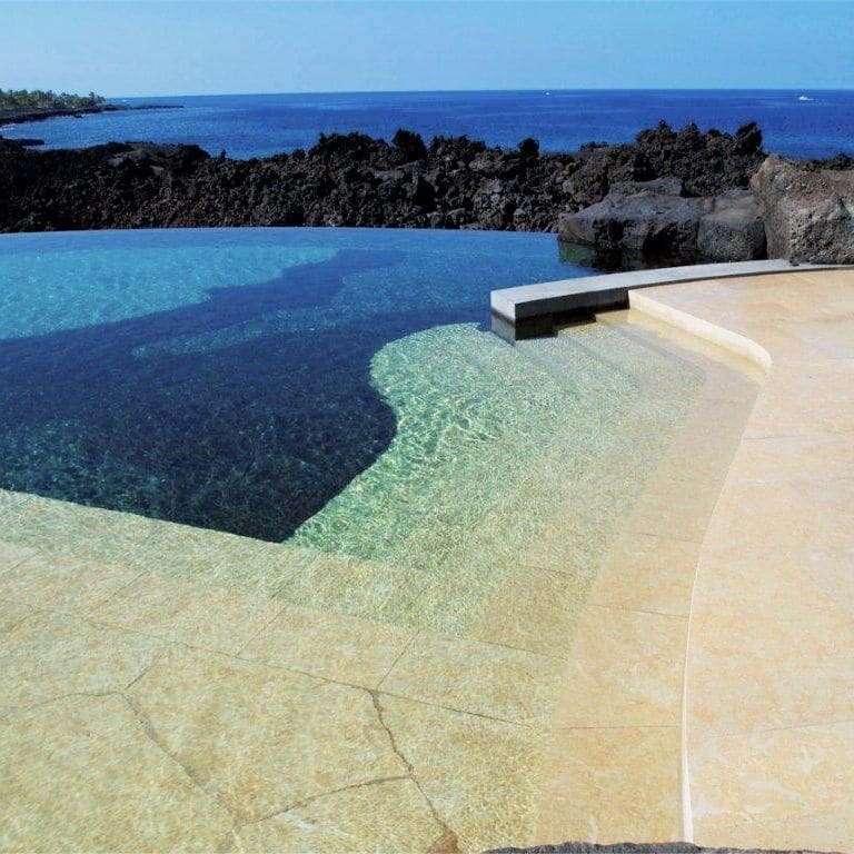 Best close-up image for Cenia Beige Limestone Pool Deck Pavers. The image shows this product being used for pool coping and pool deck pavers. The surface finish shown is flamed. Dominant colors shown are beige and tan; with orange/rust, white and cream secondaries. Exhibits "movement" and the color mix creates a warm feeling. Veined, blotched and random color patterns.