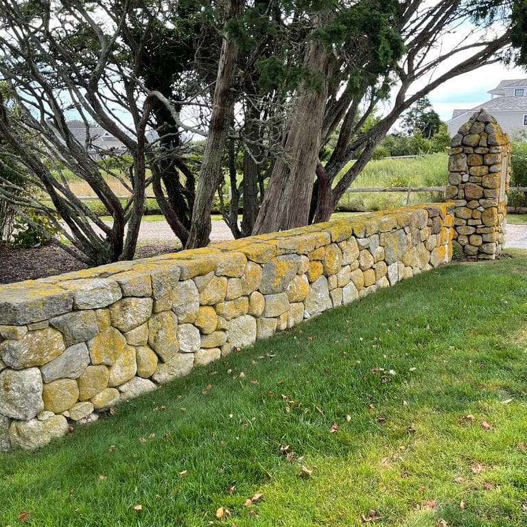 Application image for New England Fieldstone Wallstone - Light. The image shows this product being used in a landscape wallstone application. The surface finish shown is a combination of natural and weathered. The dominant color shown is gray; with tan and cream secondaries. The color mix creates a warm feeling.