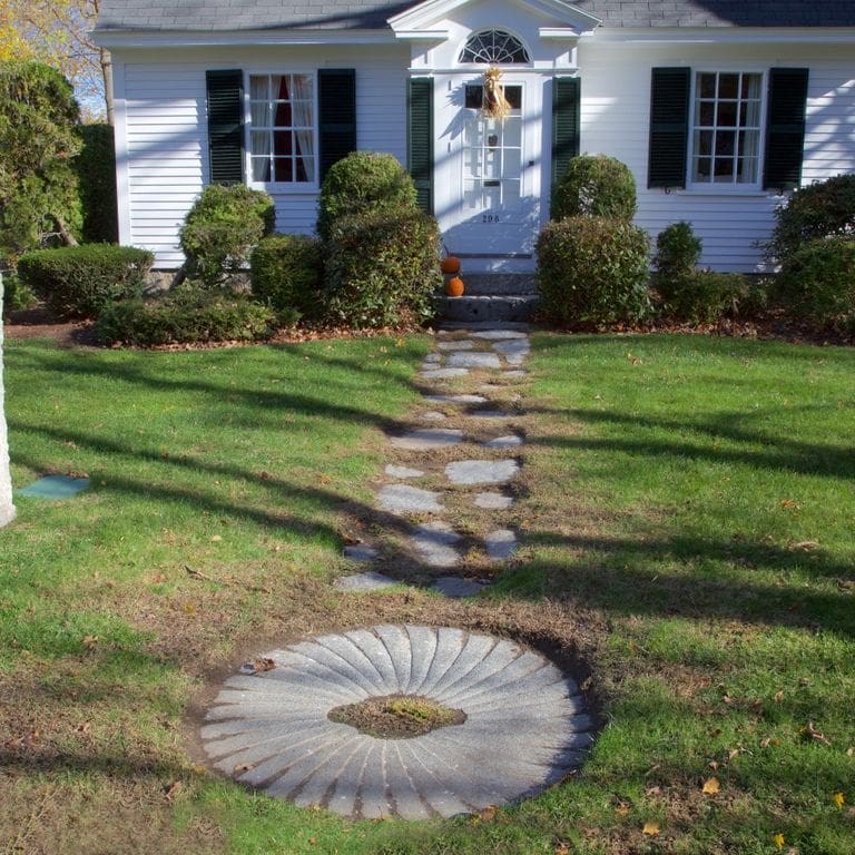 Application image for Reclaimed Antique Mill Stones. The image shows this product being used for garden accents and path pavers. The surface finish shown is a combination of carved, chiseled, weathered and worn. The dominant color shown is gray; with beige, blue, white and cream secondaries. The color mix creates a cool feeling. Regular color pattern.
