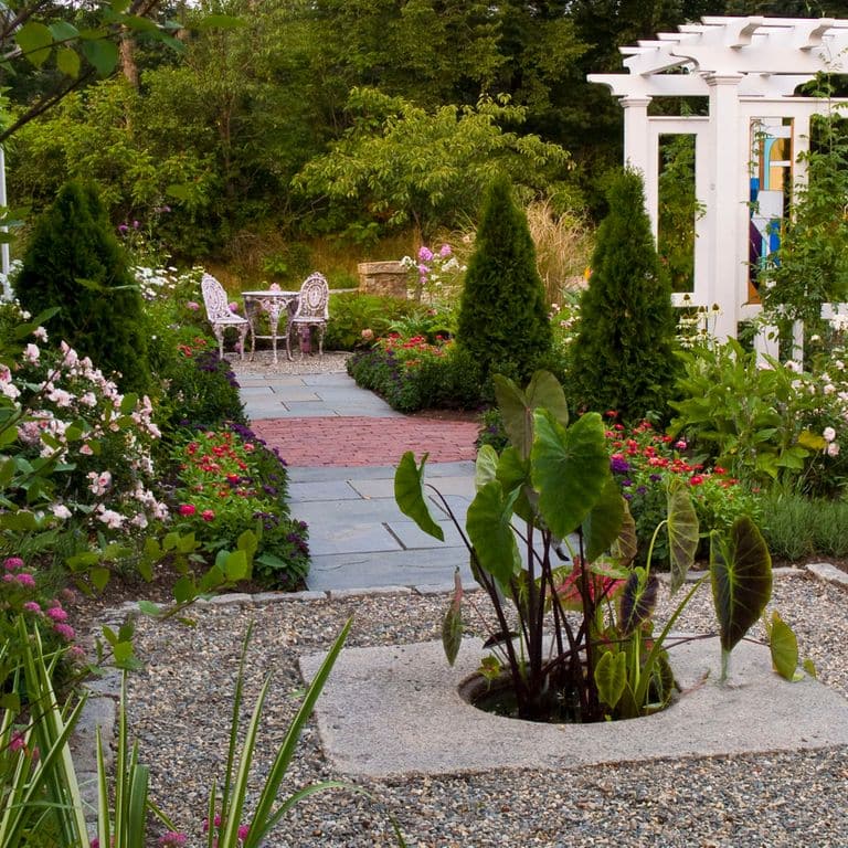 Application image for Reclaimed Granite Manhole Stones. The image shows this product being used in a garden accents application. The surface finish shown is . The dominant color shown is gray. The color mix creates a warm feeling. Fine speckled color pattern.