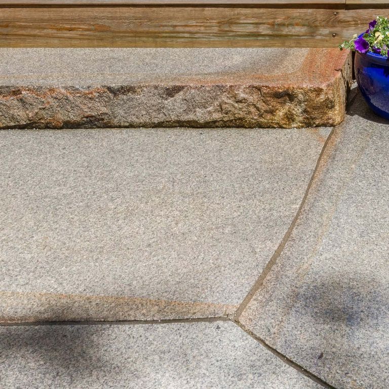 Application image for Cape Neddick Full Color Granite - Flamed Top Live Edge Steps. The image shows this product being used in a monolithic steps application. Dominant colors shown are beige and gray; with brown, orange/rust and white secondaries. Exhibits "movement" and the color mix creates a warm feeling. Fine speckled and speckled color patterns.