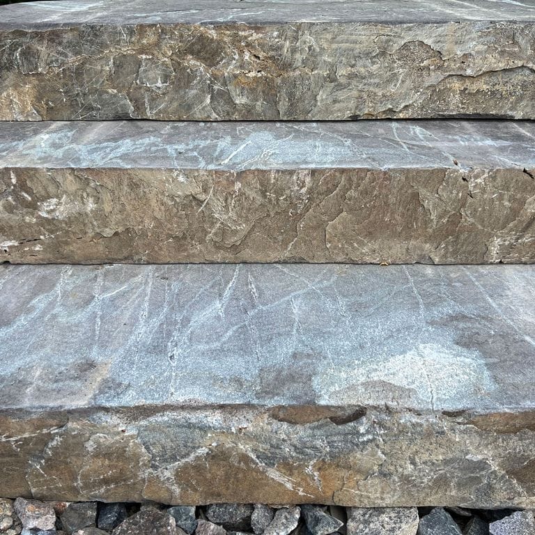 Best close-up image for Mystic Mountain Live Edge Steps - Flamed Tops. The image shows this product being used in a monolithic steps application. The surface finish shown is a combination of flamed and natural. Dominant colors shown are blue and gray; with beige, black, brown, green, orange/rust, pink, purple, white, tan and cream secondaries. Exhibits "movement". Linear, streaked and veined color patterns.
