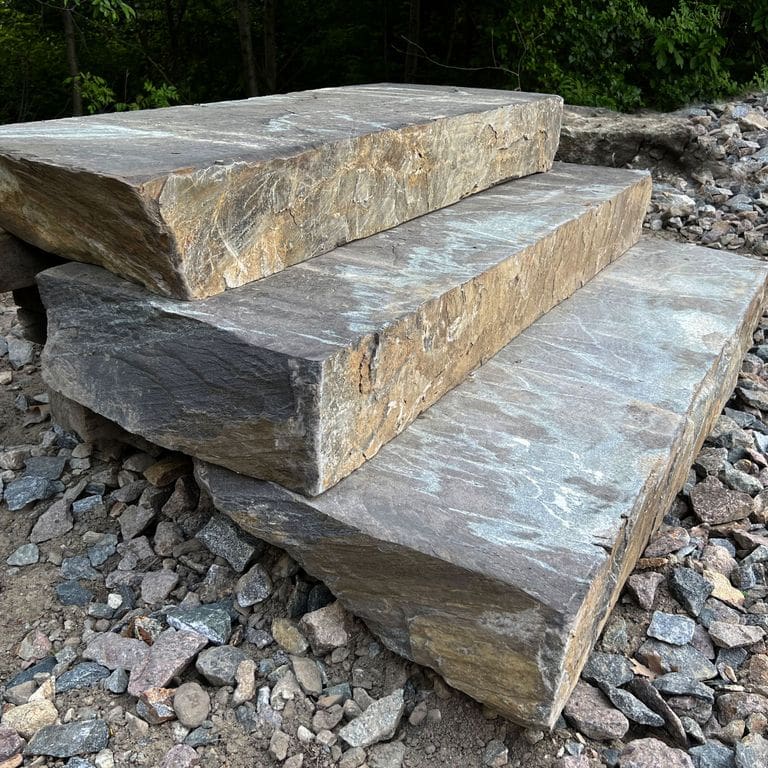 Application image for Granite - Mystic Mountain - Live Edge Steps - Flamed Tops. The image shows this product being used in a monolithic steps application. The surface finish shown is a combination of flamed and natural. The dominant color shown is gray; with beige, blue, brown, orange/rust, white, tan and cream secondaries. Exhibits "movement" and the color mix creates a warm feeling. Veined and blotched color patterns.