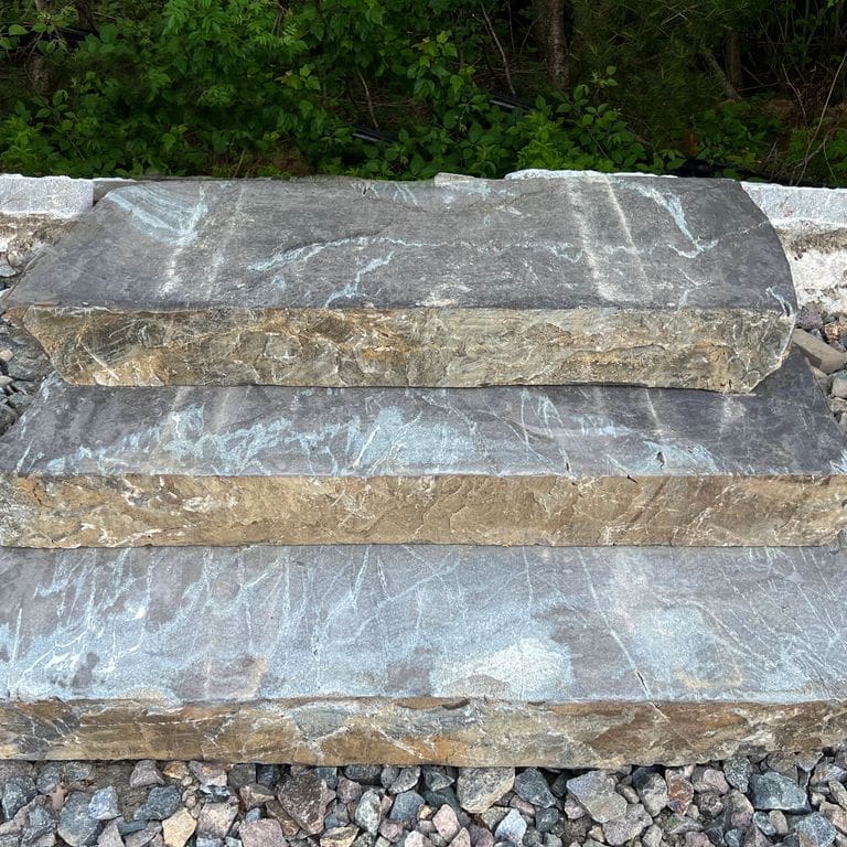 Application image for Granite - Mystic Mountain - Live Edge Steps - Flamed Tops. The image shows this product being used in a monolithic steps application. The surface finish shown is a combination of flamed and natural. Dominant colors shown are blue and gray; with beige, brown, green, orange/rust, white and tan secondaries. Exhibits "movement" and the color mix creates a warm feeling. Veined and blotched color patterns.