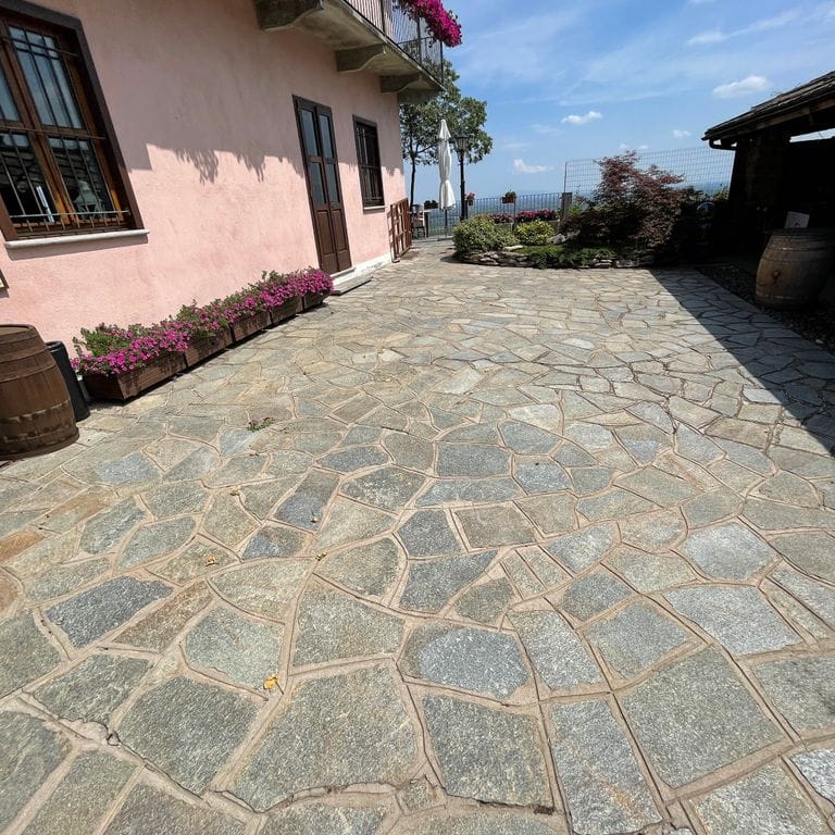 Application image for Pietra Italia Gneiss - Natural Surface Irregular Pavers. The image shows this product being used in a patio pavers application. The surface finish shown is natural cleft. Dominant colors shown are beige and gray; with brown, green, orange/rust, pink, purple, white, tan and cream secondaries. The color mix creates a warm feeling. Regular, linear and random color patterns. Contains some mica and mineral inclusions.