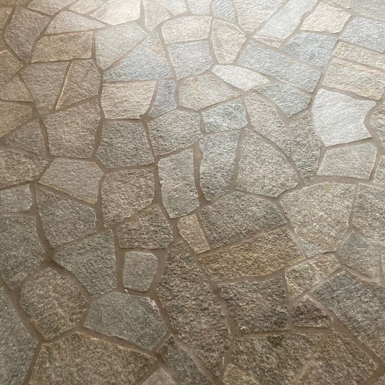 Application image for Pietra Italia Gneiss - Natural Surface Irregular Pavers. The image shows this product being used in a patio pavers application. The surface finish shown is natural cleft. Dominant colors shown are gray and tan. The color mix creates a warm feeling.