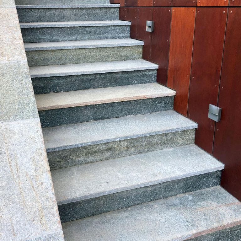 Application image for Pietra Italia Full Color Gneiss - Treads. The image shows this product being used for wallstone cap and treads. The surface finish shown is flamed. Dominant colors shown are blue and gray; with beige, green, pink, white and cream secondaries. The color mix creates a cool feeling. Regular and random color patterns. Contains some mica and mineral inclusions.