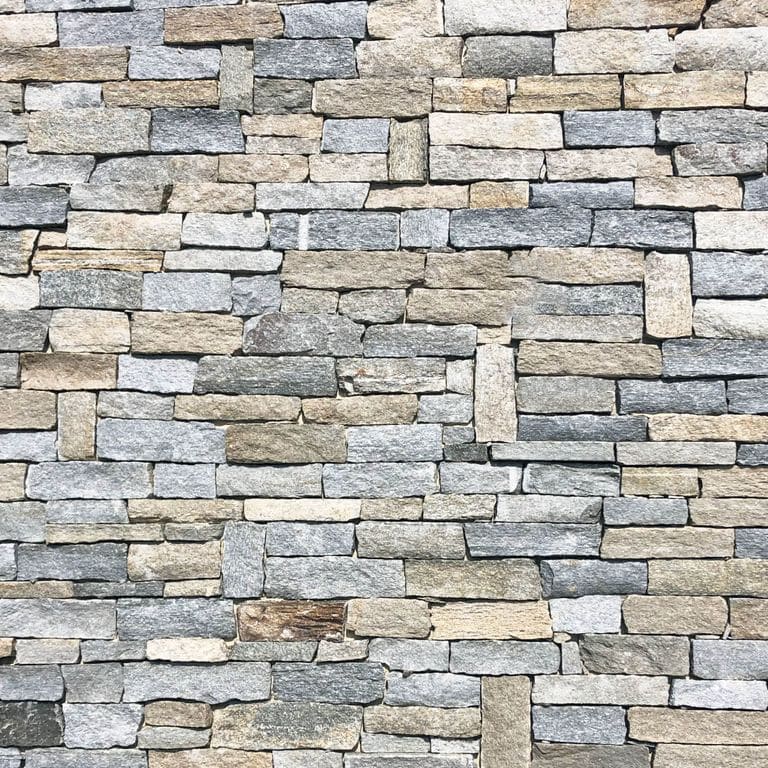 Best close-up image for Pietra Italia Gneiss - Full Color - Veneer. The image shows this product being used for full bed veneer and thin veneer. The surface finish shown is split-face. Dominant colors shown are beige, gray and tan; with black, blue, brown, orange/rust, pink, purple, white and cream secondaries. The color mix creates a warm feeling. Regular, fine speckled and random color patterns. Contains some mica and mineral inclusions.