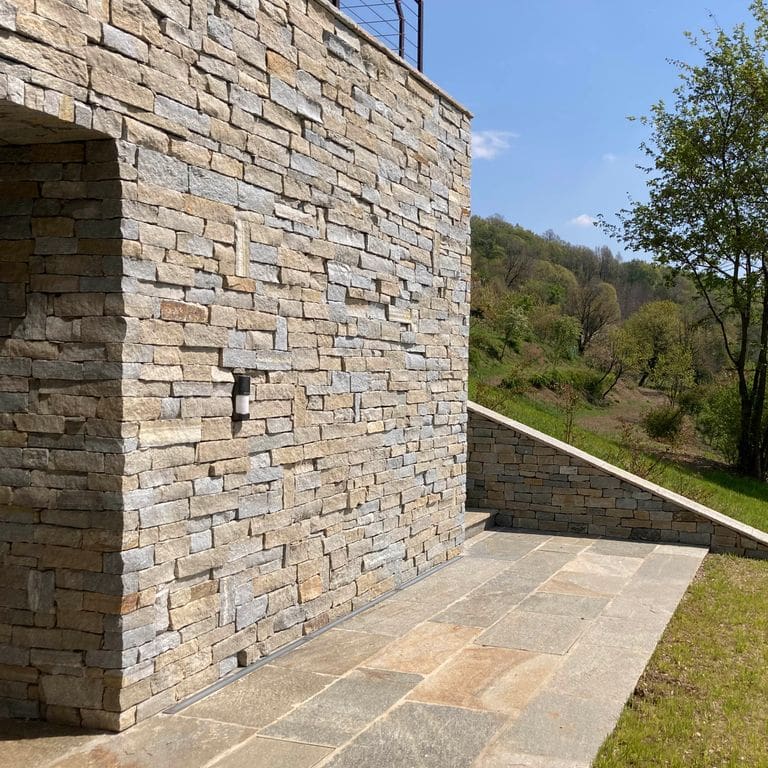 Feature image for Pietra Italia Full Color Gneiss - Veneer. The image shows this product being used for patio pavers, full bed veneer and thin veneer. The surface finish shown is split-face. Dominant colors shown are beige, gray and tan; with green, orange/rust, pink, purple, white and cream secondaries. The color mix creates a warm feeling. Regular, linear and random color patterns.