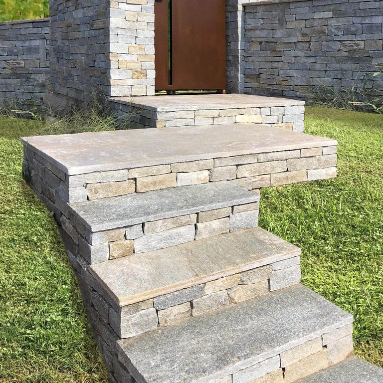 Application image for Pietra Italia Full Color Gneiss - Veneer. The image shows this product being used for treads, full bed veneer and thin veneer. The surface finish shown is split-face. Dominant colors shown are beige and gray; with orange/rust, pink, white, tan and cream secondaries. The color mix creates a warm feeling. Regular and random color patterns.