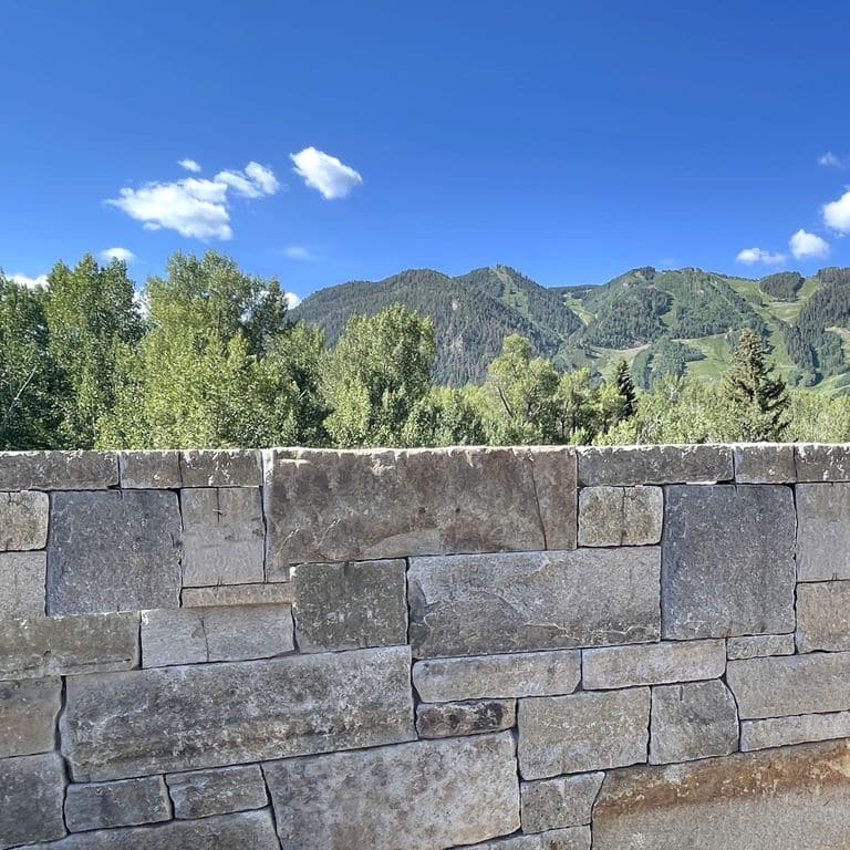 Application image for Reclaimed Granite Curbstone - Full Bed Veneer. The image shows this product being used in a full bed veneer application. Dominant colors shown are gray and tan. Exhibits "movement". Regular, linear, speckled and blotched color patterns.