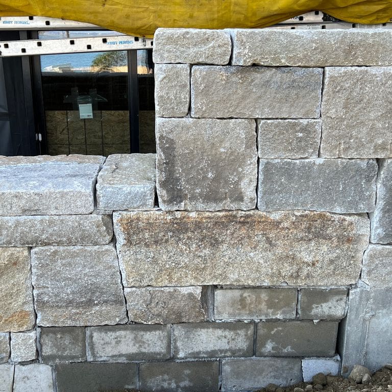 Application image for Reclaimed Granite Curbstone - Full Bed Veneer. The image shows this product being used for wallstone cap and full bed veneer. The surface finish shown is . Dominant colors shown are gray and tan. Exhibits "movement". Regular, linear and blotched color patterns.