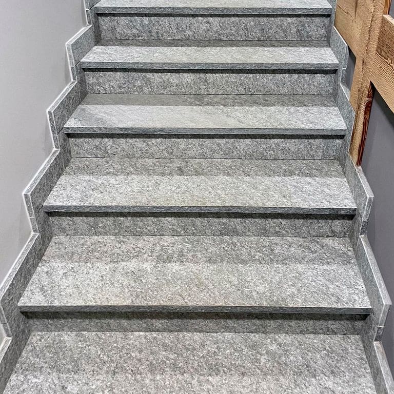 Best close-up image for Pietra Italia Full Color Gneiss - Worked Surface Treads. The image shows this product being used in a treads application. The surface finish shown is sand blasted. Dominant colors shown are beige, gray, white and tan; with blue, brown, orange/rust, pink, purple, white and cream secondaries. Regular, fine speckled and cloudy color patterns.