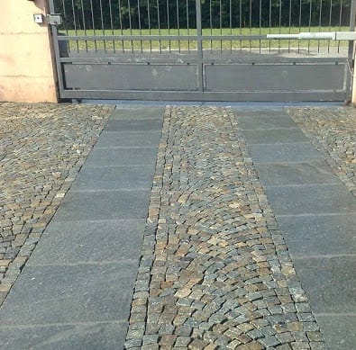 Application image for Pietra Italia Gneiss - Cobblestone Cubes. The image shows this product being used in a driveway pavers application. Dominant colors shown are gray and tan.