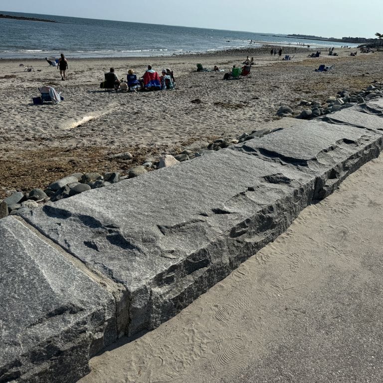 Best close-up image for Granite - Dodlin Hill - Bridge Block. The image shows this product being used in a retaining wall application. The surface finish shown is natural cleft. Dominant colors shown are blue and gray. The color mix creates a cool feeling.