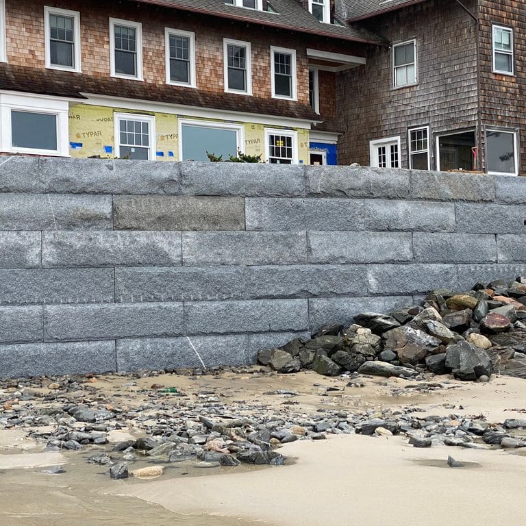 Feature image for Granite - Dodlin Hill - Bridge Block. The image shows this product being used in a retaining wall application. The surface finish shown is natural cleft. The dominant color shown is gray. The color mix creates a warm feeling.