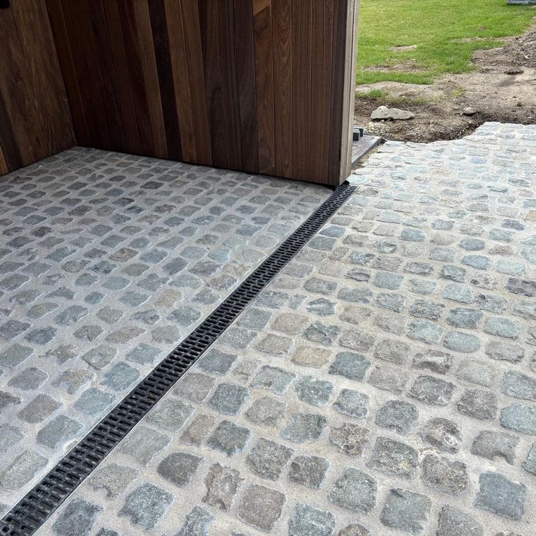 Application image for Reclaimed European Porphyry Cobblestones - Square - Worn Surface. The image shows this product being used in a driveway pavers application. The surface finish shown is . The dominant color shown is gray. The color mix creates a cool feeling.
