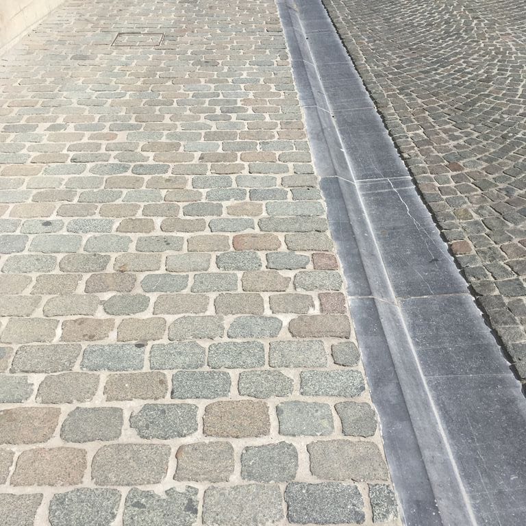 Application image for Porphyry - Reclaimed European Cobblestone - Rectangle - Flat Surface. The image shows this product being used in a path pavers application. Dominant colors shown are gray and tan. Fine speckled color pattern.