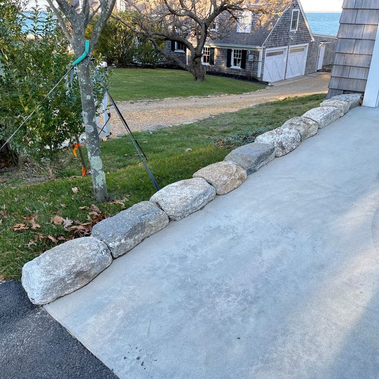 Feature image for Fieldstone - New England Rounds - Edging . The image shows this product being used in a landscape curbing &amp; edging application. The surface finish shown is . The dominant color shown is gray. The color mix creates a cool feeling.
