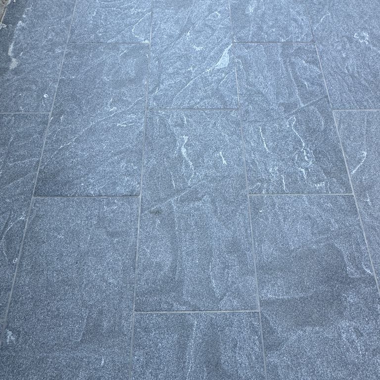 Best close-up image for Granite - Jet Mist - Pavers. The image shows this product being used in a patio pavers application. The surface finish shown is flamed. The dominant color shown is gray.