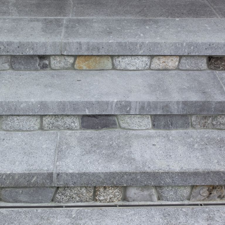 Close-up image for Oak Mountain Granite Treads. The surface finish shown is flamed. Dominant colors shown are blue and gray; with a white secondary. The color mix creates a cool feeling. Regular, speckled and fine speckled color patterns. Contains mineral inclusions.
