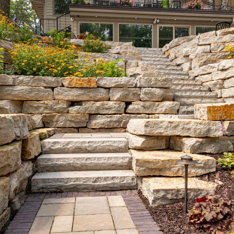 Feature image for Rustic Gold Limestone - Wallstone. The image shows this product being used for landscape wallstone and monolithic steps. The surface finish shown is natural cleft. Dominant colors shown are orange/rust, yellow and tan. The color mix creates a warm feeling.