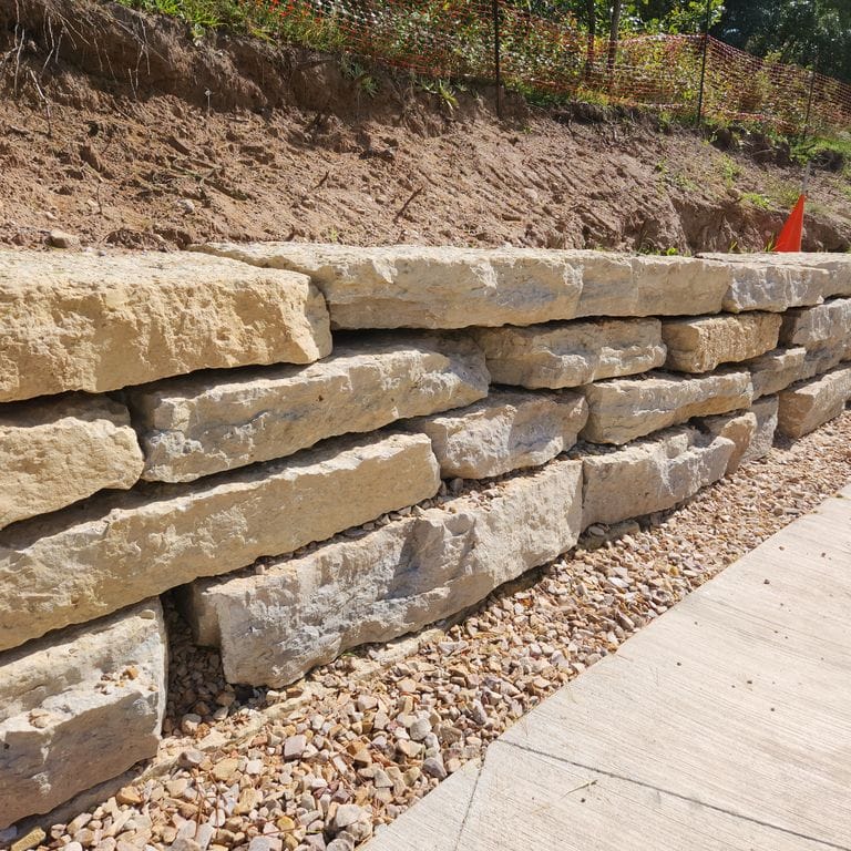 Application image for Rustic Gold Limestone - Wallstone. The image shows this product being used for landscape wallstone and retaining wall. The surface finish shown is natural cleft. Dominant colors shown are yellow, tan and cream. The color mix creates a warm feeling.